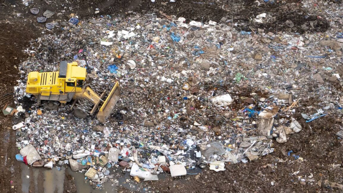 Aerial view of a landfill site with large amounts of trash and a vehicle with a plow